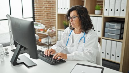 Foto de Médico hispano de mediana edad usando computadora trabajando en la clínica - Imagen libre de derechos