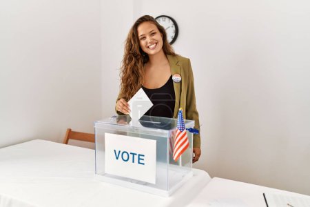 Foto de Joven mujer hispana hermosa mesa electoral presidente poniendo voto en caja en colegio electoral - Imagen libre de derechos