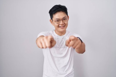 Photo for Young asian man standing over white background pointing to you and the camera with fingers, smiling positive and cheerful - Royalty Free Image