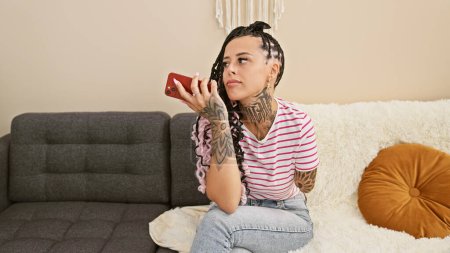 Foto de Molestar a la amputada hispana en casa, dudando mientras escribe un mensaje en su teléfono inteligente - Imagen libre de derechos