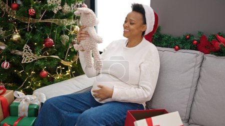 Photo for Young pregnant woman celebrating christmas holding teddy bear at home - Royalty Free Image