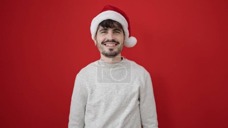Photo for Young hispanic man smiling confident wearing christmas hat over isolated red background - Royalty Free Image