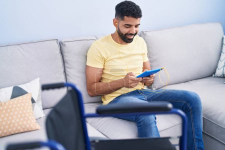 Foto de Hombre árabe joven usando touchpad sentado en el sofá en casa - Imagen libre de derechos