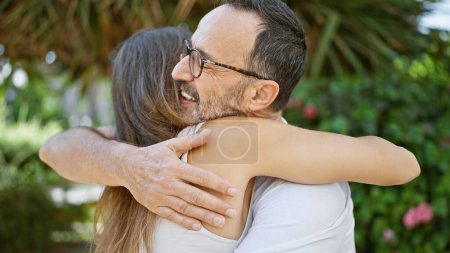 Foto de En el soleado parque, un padre confiado comparte un abrazo alegre y sonriente con su encantadora hija, una dulce expresión de amor familiar y felicidad al aire libre. - Imagen libre de derechos