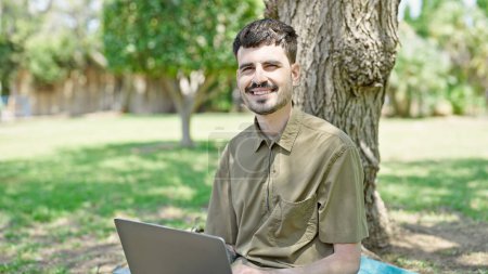 Photo for Young hispanic man using laptop sitting on floor smiling at park - Royalty Free Image