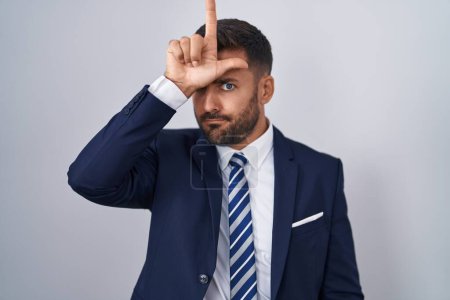 Photo for Handsome hispanic man wearing suit and tie making fun of people with fingers on forehead doing loser gesture mocking and insulting. - Royalty Free Image