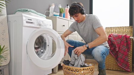 Photo for Young hispanic man washing clothes listening to music at laundry room - Royalty Free Image
