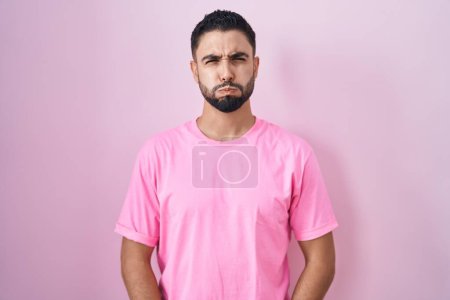 Foto de Joven hispano de pie sobre fondo rosa hinchando mejillas con cara divertida. boca hinchada de aire, expresión loca. - Imagen libre de derechos