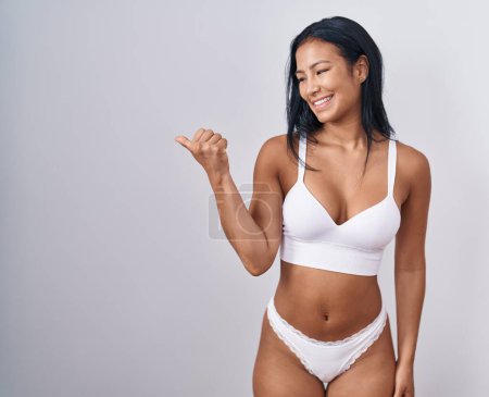 Photo for Hispanic woman wearing lingerie smiling with happy face looking and pointing to the side with thumb up. - Royalty Free Image