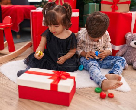 Photo for Brother and sister playing with toys sitting on floor by christmas gifts at home - Royalty Free Image