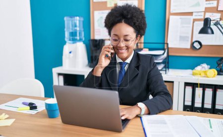 Téléchargez les photos : Femme afro-américaine travailleur d'affaires en utilisant un ordinateur portable parlant sur smartphone au bureau - en image libre de droit