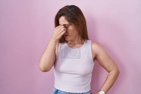 Photo for Brunette woman standing over pink background tired rubbing nose and eyes feeling fatigue and headache. stress and frustration concept. - Royalty Free Image