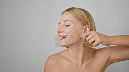 Téléchargez les photos : Jeune femme blonde massant le visage à l'aide de quartz rose gua sha sur fond blanc isolé - en image libre de droit
