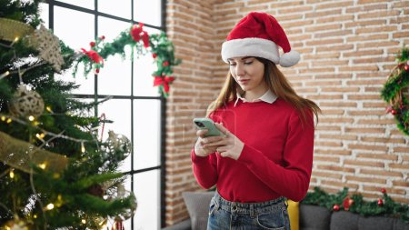Photo for Young hispanic woman celebrating christmas using smartphone at home - Royalty Free Image