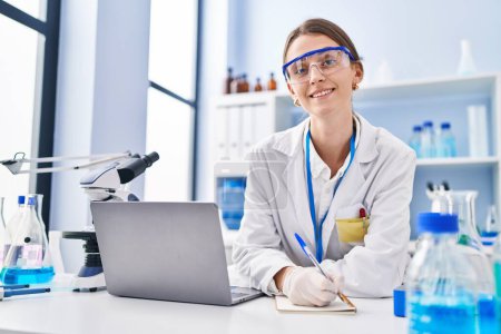 Foto de Mujer joven caucásica científico utilizando la escritura portátil en el portátil en el laboratorio - Imagen libre de derechos