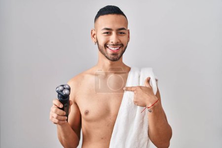 Téléchargez les photos : Jeune homme hispanique tenant un rasoir électrique pointant du doigt un sourire heureux et fier - en image libre de droit