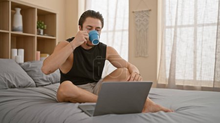 Foto de Joven hispano usando laptop bebiendo café en el dormitorio - Imagen libre de derechos