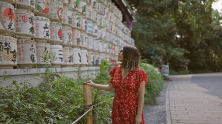Téléchargez les photos : Belle femme hispanique souriante, debout par barils secoués au temple meiji tout en embrassant la culture japonaise, tout en enfilant des lunettes - en image libre de droit