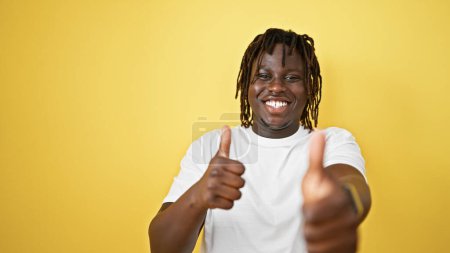 Foto de Hombre afroamericano sonriendo con pulgares hacia arriba sobre fondo amarillo aislado - Imagen libre de derechos