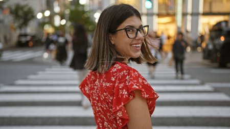 Photo for Beautiful hispanic woman in glasses, smiling and looking back at camera, walking across tokyo street crosswalk - Royalty Free Image
