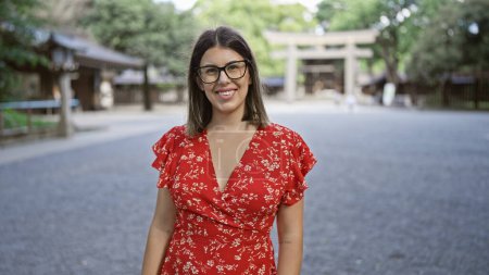 Téléchargez les photos : Joyeux, belle femme hispanique avec des lunettes pose avec confiance, souriant au sanctuaire meiji de tokyo, sa joie rayonnant sans équivoque à travers son sourire étonnant - en image libre de droit