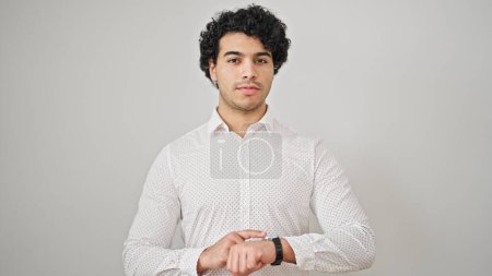 Foto de Joven trabajador de negocios latino tocando reloj con expresión seria sobre fondo blanco aislado - Imagen libre de derechos