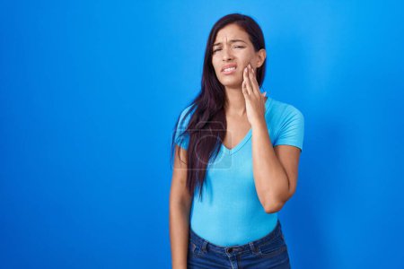 Téléchargez les photos : Jeune femme hispanique debout sur fond bleu touchant la bouche avec la main avec une expression douloureuse à cause de maux de dents ou de maladies dentaires sur les dents. dentiste - en image libre de droit