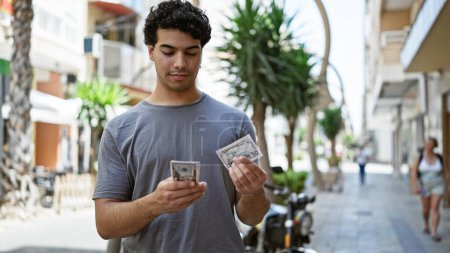 Téléchargez les photos : Jeune homme latin comptant les dollars à la rue - en image libre de droit