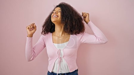 Téléchargez les photos : Femme afro-américaine souriante debout avec confiance geste gagnant sur fond rose isolé - en image libre de droit