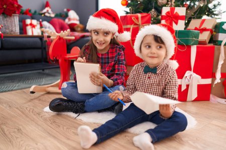Foto de Adorable niño y niña dibujando en papel celebrando la Navidad en casa - Imagen libre de derechos