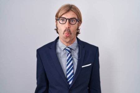 Foto de Hombre caucásico con bigote usando ropa de negocios haciendo cara de pez con labios, gesto loco y cómico. expresión divertida. - Imagen libre de derechos