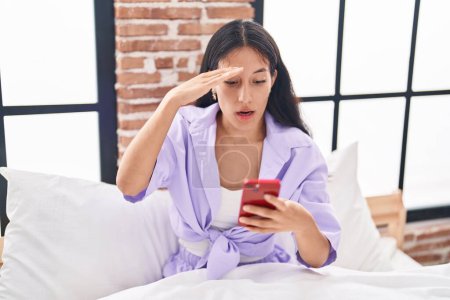 Photo for Young beautiful hispanic woman using smartphone with worried expression at bedroom - Royalty Free Image