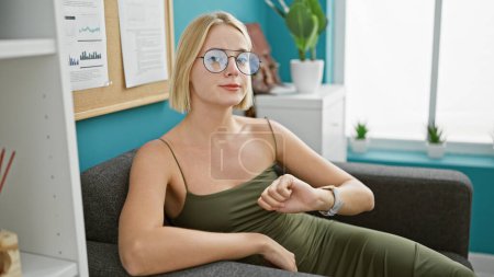 Téléchargez les photos : Jeune femme blonde ouvrière regardant la montre avec un visage sérieux au bureau - en image libre de droit