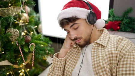 Téléchargez les photos : Jeune homme arabe dormant sur le canapé près de l'arbre de Noël à la maison - en image libre de droit