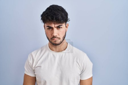 Foto de Hombre hispano con barba de pie sobre fondo blanco escéptico y nervioso, frunciendo el ceño molesto debido a un problema. persona negativa. - Imagen libre de derechos