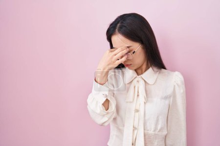 Foto de Mujer joven china de pie sobre fondo rosa cansada frotando la nariz y los ojos sintiendo fatiga y dolor de cabeza. concepto de estrés y frustración. - Imagen libre de derechos