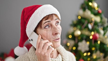 Foto de Mujer hispana madura hablando por teléfono junto al árbol de Navidad en casa - Imagen libre de derechos