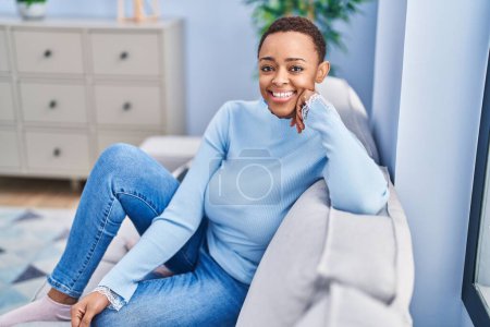 Foto de Mujer afroamericana sonriendo confiada sentada en el sofá en casa - Imagen libre de derechos