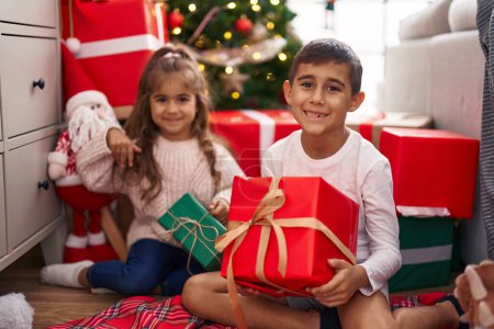 Foto de Hermano y hermana sosteniendo regalo sentado en el suelo por regalos de Navidad en casa - Imagen libre de derechos