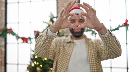 Photo for Young hispanic man doing heart gesture celebrating christmas at home - Royalty Free Image