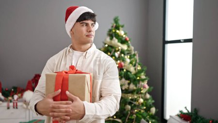 Photo for Young hispanic man holding christmas gift at home - Royalty Free Image