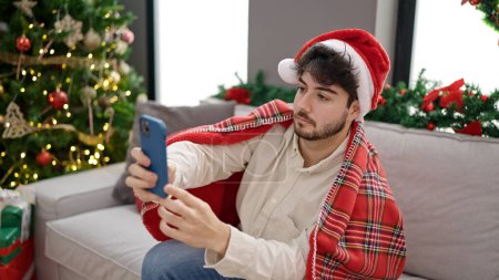 Téléchargez les photos : Jeune homme hispanique célébrant Noël faire selfie photo par smartphone à la maison - en image libre de droit