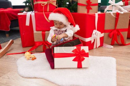 Photo for Adorable blonde toddler unpacking gift sitting by christmas tree at home - Royalty Free Image