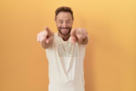 Photo for Middle age man with beard standing over yellow background pointing to you and the camera with fingers, smiling positive and cheerful - Royalty Free Image