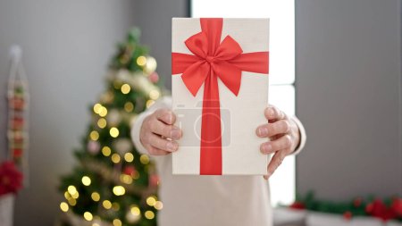Téléchargez les photos : Moyen Age homme aux cheveux gris tenant cadeau de Noël sur le visage à la maison - en image libre de droit