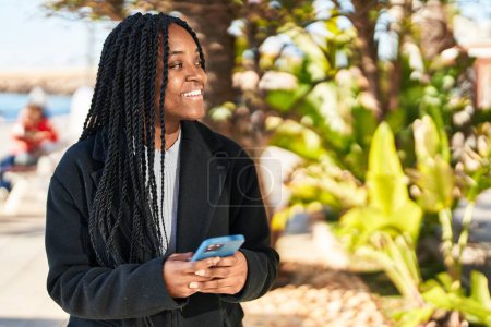 Téléchargez les photos : Femme afro-américaine souriante confiante en utilisant un smartphone au parc - en image libre de droit