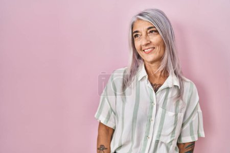 Téléchargez les photos : Femme d'âge moyen avec les cheveux gris debout sur fond rose regardant de côté avec le sourire sur le visage, expression naturelle. riant confiant. - en image libre de droit