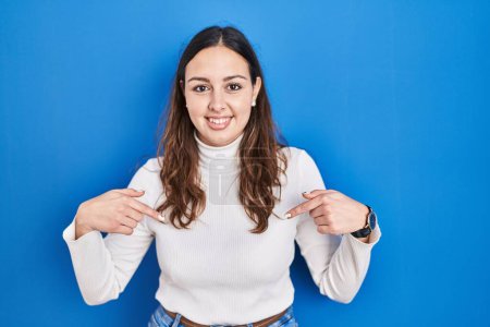 Photo for Young hispanic woman standing over blue background looking confident with smile on face, pointing oneself with fingers proud and happy. - Royalty Free Image