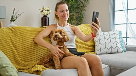 Téléchargez les photos : Jeune femme caucasienne avec chien faire appel vidéo assis sur le canapé à la maison - en image libre de droit