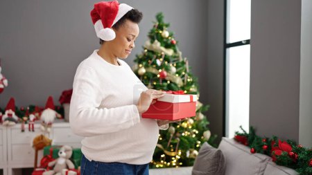 Photo for Young pregnant woman celebrating christmas unpacking gift at home - Royalty Free Image